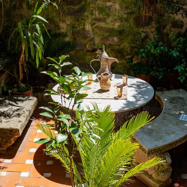 Ein sonniger Innenhof mit einem runden Tisch, Pflanzen und einer dekorativen Vase.